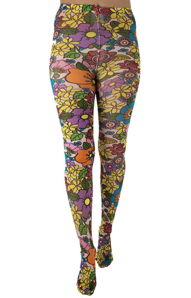 A model wearing tights printed with an all-over pattern of retro illustrations of multicolored yellow, purple, blue, green, red, and pink flowers with black outlines on a pale blush pink background. Shown from the front 