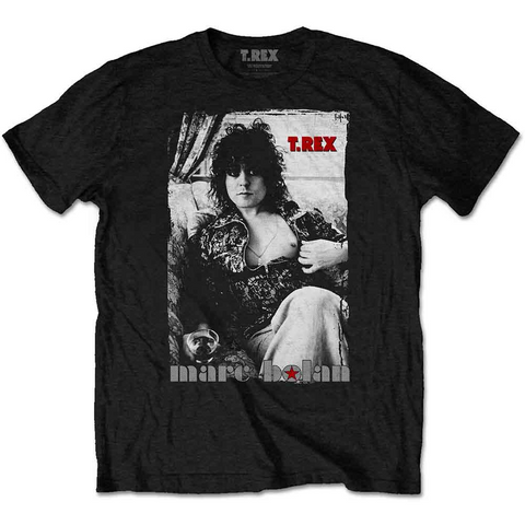 Black short sleeve t shirt with black and white image of Marc Bolan sitting on a couch holding a glass of liquor and holding his zip up shirt open to expose a single nipple. T. REX is written in red beside his head and “marc bolan” is written underneath the image with a red star inside the letter O