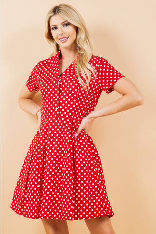 A model wearing a red and white polka dot patterned cotton shirt-waist dress with white pearly plastic buttons, short sleeves, and a flared above the knee skirt. Shown from the front