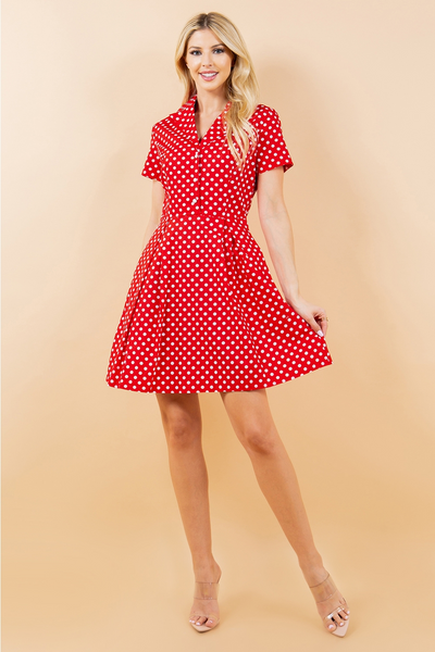 A model wearing a red and white polka dot patterned cotton shirt-waist dress with white pearly plastic buttons, short sleeves, and a flared above the knee skirt. Shown from the front with skirt held flared