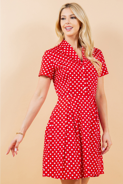 A model wearing a red and white polka dot patterned cotton shirt-waist dress with white pearly plastic buttons, short sleeves, and a flared above the knee skirt. Shown from the front in a three quarter angle