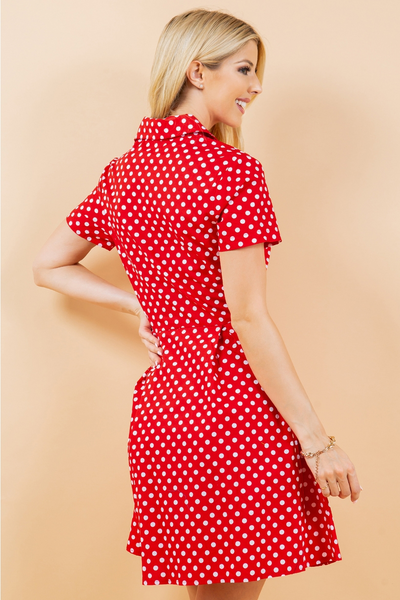 A model wearing a red and white polka dot patterned cotton shirt-waist dress with white pearly plastic buttons, short sleeves, and a flared above the knee skirt. Shown from the back