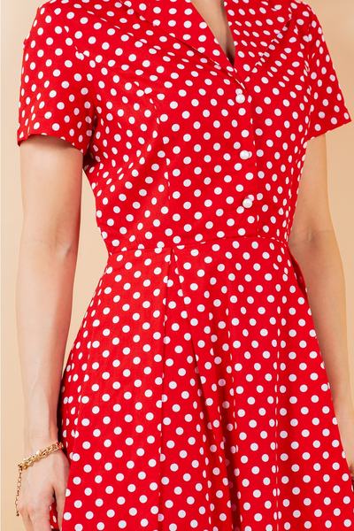 A model wearing a red and white polka dot patterned cotton shirt-waist dress with white pearly plastic buttons, short sleeves, and a flared above the knee skirt. Shown from the front in close up