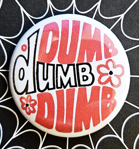 1.25 round button with white background and “DUMB dumb DUMB” written in black and red surrounded by red and black cartoon flowers