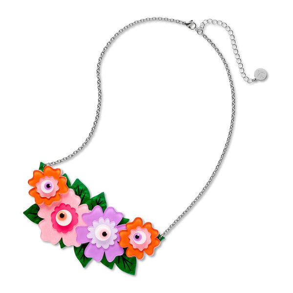 A colorful floral necklace with four stylized flowers in orange, pink, and purple, all with eyeball centers, and accented with green leaves and a silver chain