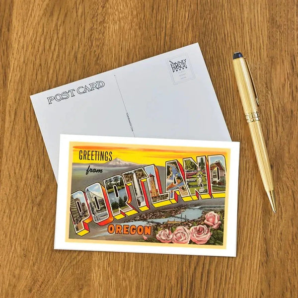 Postcard with 'Greetings from Portland, Oregon' design on a wooden surface with a pen.