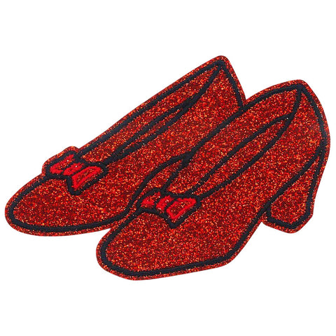 Embroidered patch of ruby red slippers shown from a three quarter angle as seen in The Wizard of Oz on bright red glittery fabric