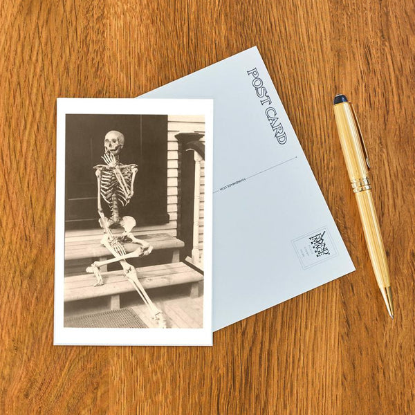 Skeletal figure on a bench postcard with a pen on a wooden surface