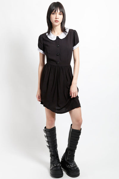 model wearing black rayon shirtwaist dress with white lace peter pan collar, matching lace cuffs at short sleeves, round black plastic buttons at bodice and gathered above the knee skirt. Shown from front