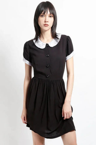 model wearing black rayon shirtwaist dress with white lace peter pan collar, matching lace cuffs at short sleeves, round black plastic buttons at bodice and gathered above the knee skirt. Shown from front in close up