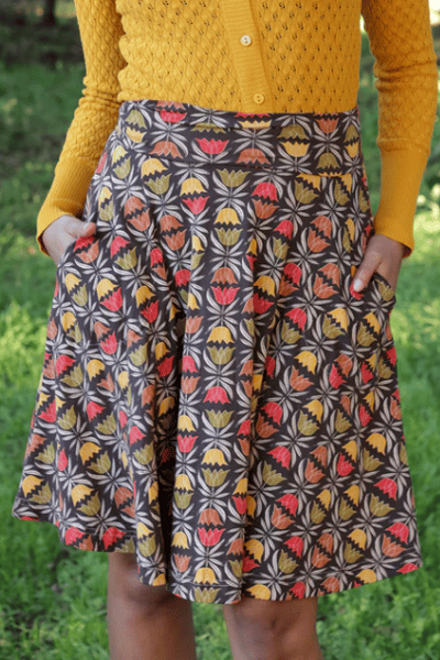 stretch cotton knit high-waisted just-above-the-knee length flared skirt in a burgundy background with repeat tessellated burnt orange, yellow, green, and cream stylized tulip pattern. shown worn by a model