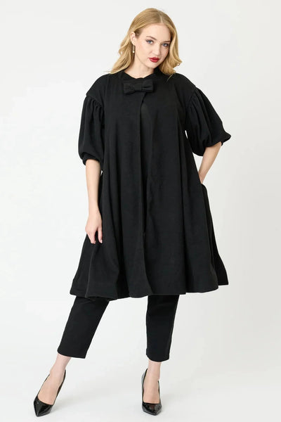  1960s style black swing coat with bow detail at the neck, and puffed 1/2 sleeves, worn by a model