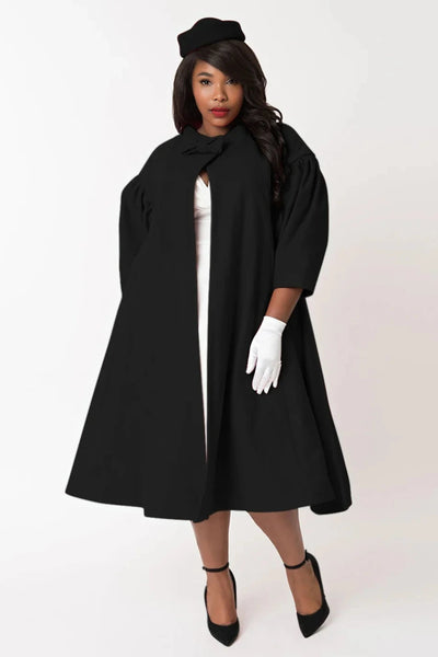  1960s style black swing coat with bow detail at the neck, and puffed 1/2 sleeves, worn by a model