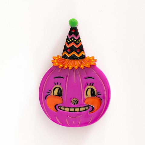 layered acrylic resin brooch of a bright fuchsia colored pumpkin with black details and orange cheeks wearing a glittery orange, yellow, green and black party hat. Shown flat