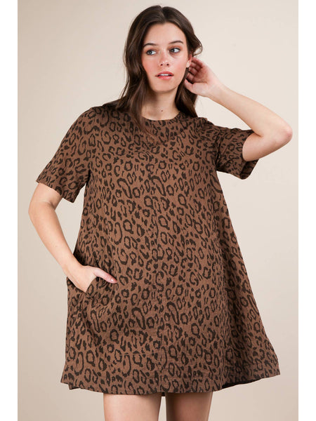 Model wearing a brown leopard print short sleeved a-line mini dress with a rounded collar and side seam pockets. Shown from the front with one hand in side seam pocket