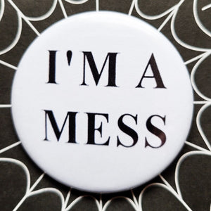1.25” white pinback button with “I’M A MESS” written in black