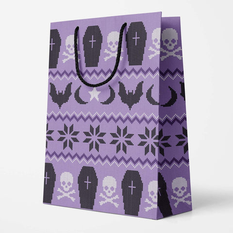 Rectangular gift bag in an all-over Fair Isle style sweater pattern with a purple background and black & white coffins, skulls, moons, stars, and bats. Bag has black polyester rope handle