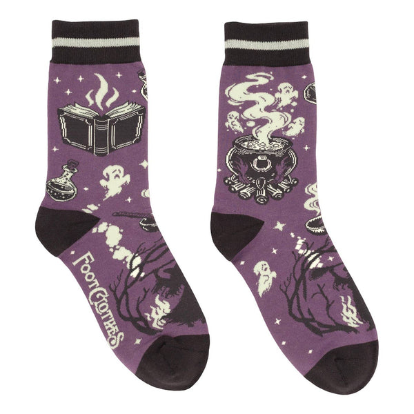 unisex cotton blend crew socks in medium purple with black toes, heels, and black & cream striped cuffs with purple, black, and cream design of spell books, bubbling cauldrons, bottles of potions, ghosts, and a witch holding a broom. Shown flat