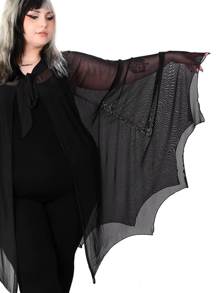 Plus size model wearing a black mesh cape with raw scalloped hemline in the shape of bat wings with sewn in arm holes and a self adjustable front tie. Shown from the front in close up of sleeve 