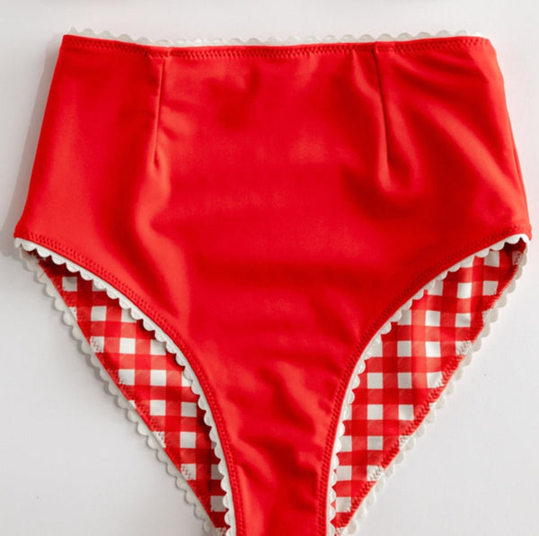 red and white gingham print reversible high waisted bikini bottoms with white rickrack style trim. Shown flat with solid red side shown