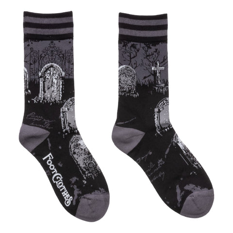 black and grey unisex crew socks with a knit in pattern of an old and overgrown graveyard with tombstones and an iron fence. With black and grey striped cuffs and grey toes/heels. Shown flat