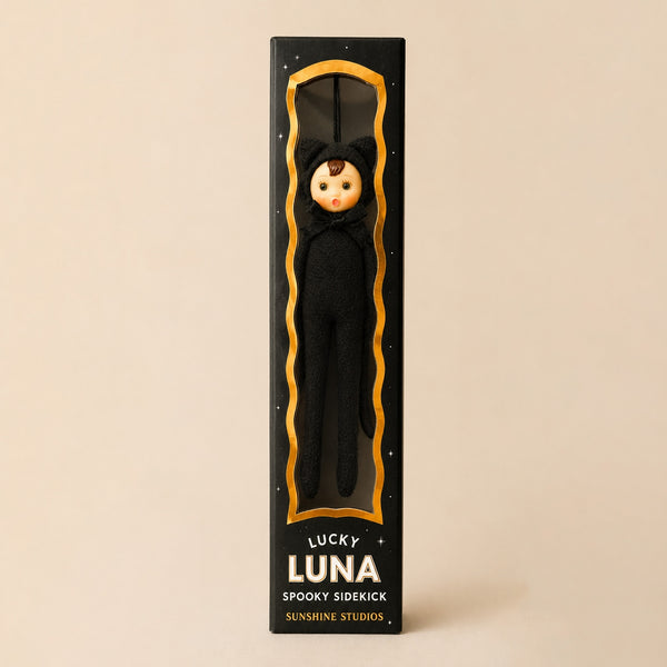 Poseable ornament with wire limbs and Velcro hands in the shape of a pixie with rosy cheeked, green eyed resin face with molded tuft of brown hair. She is wearing a black faux fur black cat costume with ears and tail. Black satin ribbon for hanging is at top of head. Shown in illustrated gift box from front