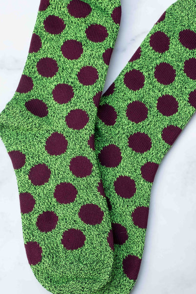 bright green heathered socks with dark wine purple polka dots on a marble background shown in close up