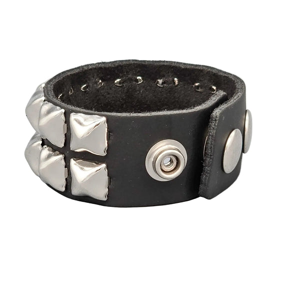 A 1 1/4” black leather cuff with two rows of 1/2” silver pyramid studs and double snap closure. Shown from snap closure side