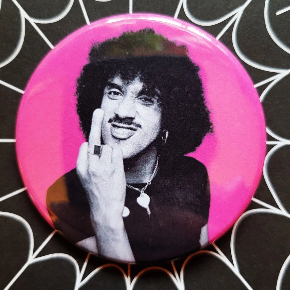 2.25” button of Phil Lynott from Thin Lizzy flipping the bird in front of a neon pink background 