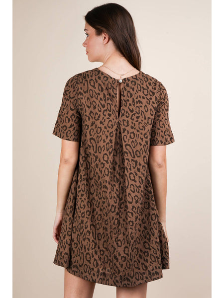 Model wearing a brown leopard print short sleeved a-line mini dress with a rounded collar and side seam pockets. Shown from the back to display pleated back detail and buttoned keyhole at back of neck