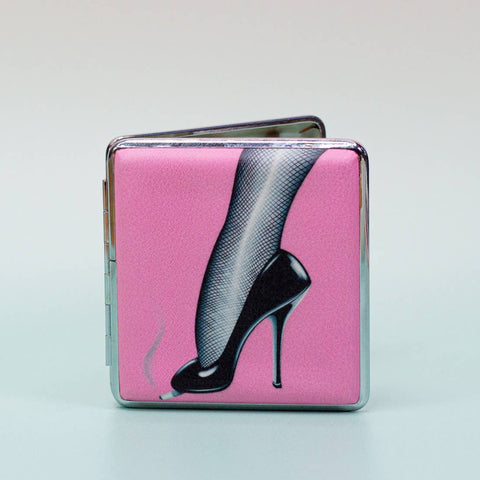 Square metal cigarette case with a printed pink front and black and white image of a high heeled shoe with fishnets stubbing out a cigarette. Shown open from the front 