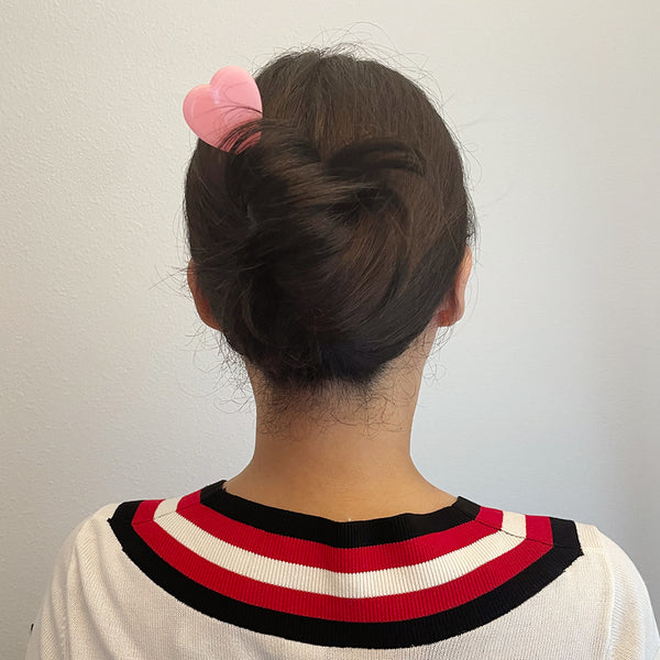 Acetate hair stick with a heart shaped topper in a shade of pink. Shown in a models hair from the back