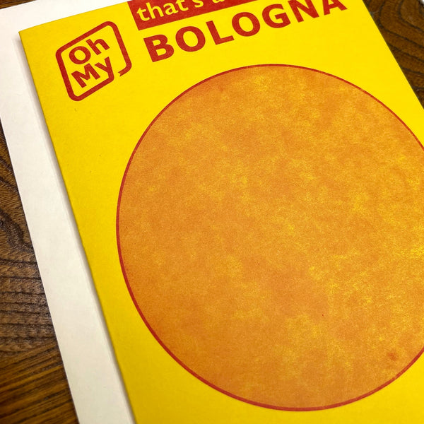 Bright yellow notecard resembling Oscar Meyer bologna package with round image of sandwich meat and message “Oh My” “that’s a bunch of BOLOGNA” “Any Way You Slice It”. Shown on wooden background in close up of print