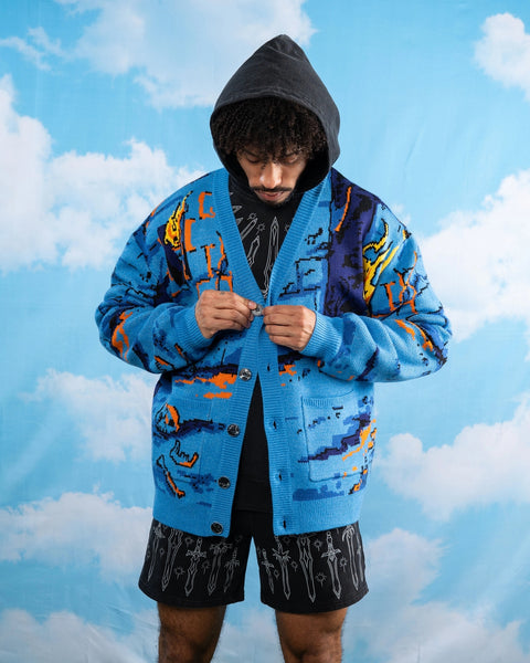 relaxed fit cardigan with jacquard knit pattern of 8-bit style pixelated dungeon design with bones, brick wall, and orange ooze on ground. Sweater has patch pockets, v-neckline, tortoiseshell buttons, and ribbed collar and cuffs. Shown on model