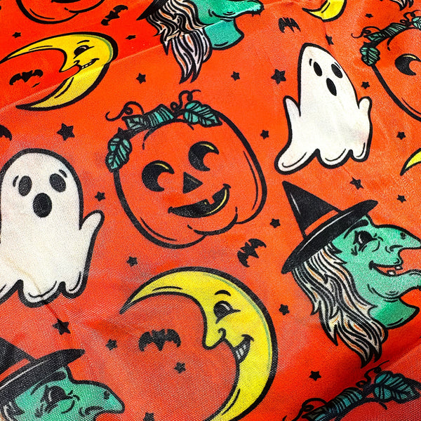An orange reusable nylon tote bag with an all-over pattern of cartoonish retro Halloween witches, ghosts, crescent moons, and jack-o'-lanterns shown in close up of pattern