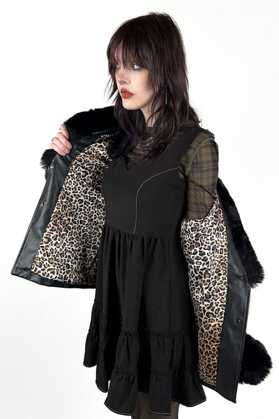 model wearing a black faux-leather wrap coat with a large black faux fur shawl collar, matching fur-trimmed cuffs, and a self-tie belt. Shown from front open to display leopard print satin lining