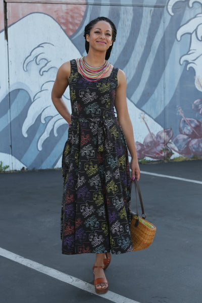 Woman wearing black print sundress standing on a street with a colorful mural in the background