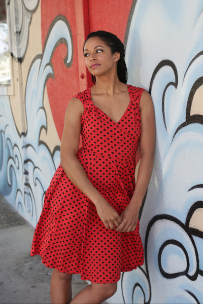 bright red stretch cotton sleeveless fit and flare dress in an allover printed black polka dot pattern featuring a surplice bodice with Queen Anne neckline, gathered wide straps and full knee length skirt. shown worn by a model