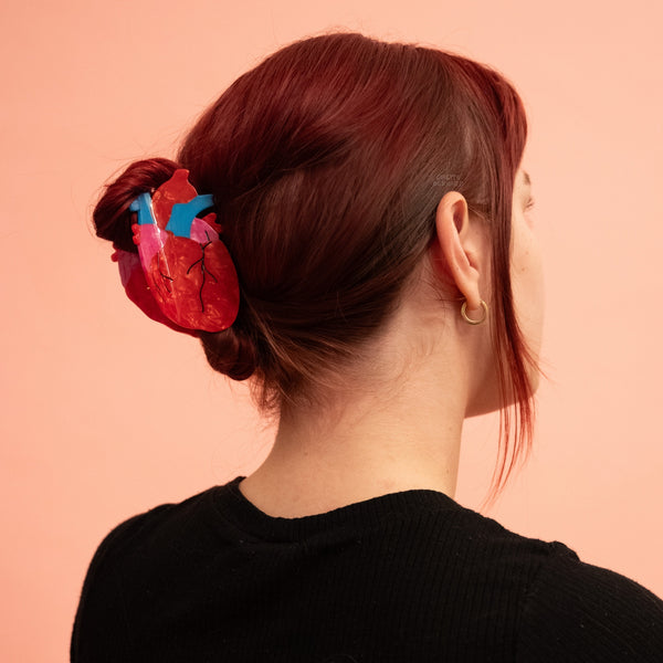 bioacetate claw style hair clip in the shape of an anatomical heart in marbled red and pink & solid blue with black line detail. Shown in model's updo from the back