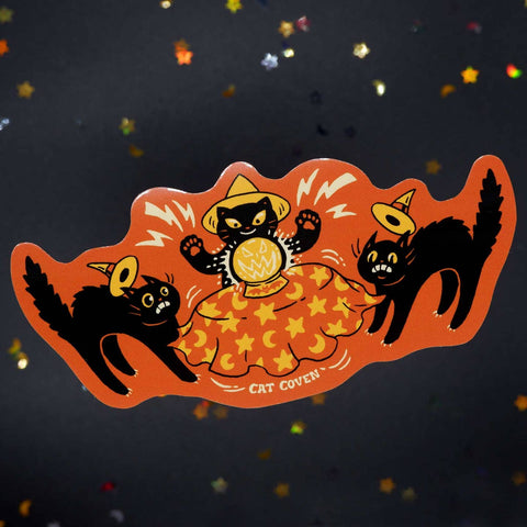 die-cut vinyl sticker with orange background of three black cats wearing yellow and orange witch hats gathered around a crystal ball, with one cat summoning pumpkin-shaped spirit and scaring the other two cats with arched backs