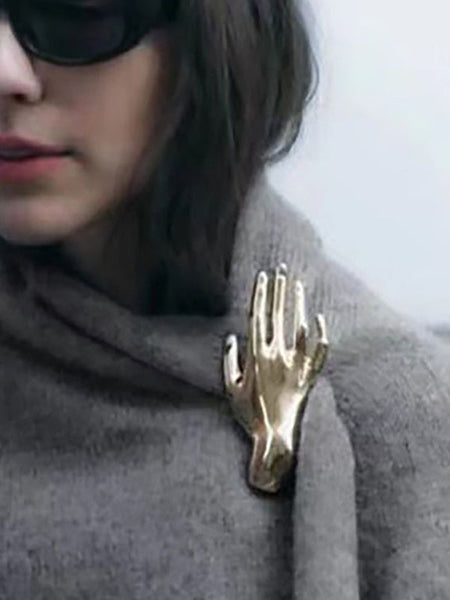 Silver metal brooch of an outstretched hand. Shown pinned to a shawl