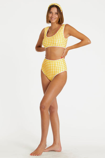 model wearing yellow and white gingham print reversible bikini. Top has scoop neckline and white rickrack style trim. Shown from side with gingham side worn