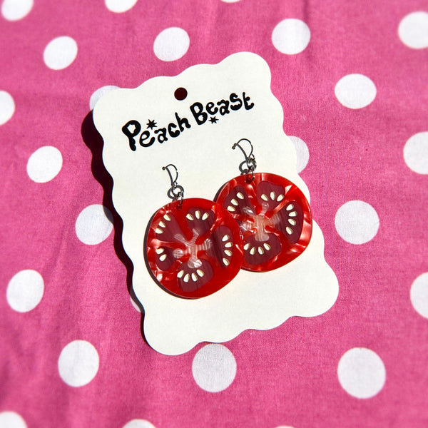 pair of marbled acrylic dangle earrings in the shape of slices of red tomato with seeds. Shown flat on backing card