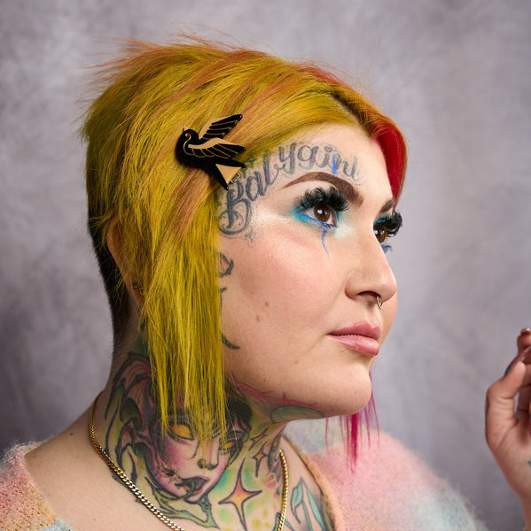 model wearing black and gold acetate sparrow shaped barrette with gold jewel eyes.