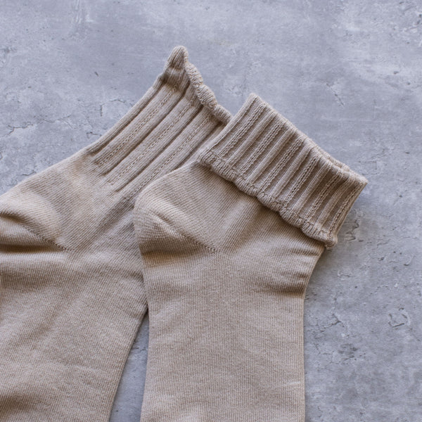 Light beige cotton knit socks with ribbed pattern and scalloped cuffs. Shown flat in close up with cuff folded