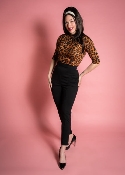 model wearing a pair of black knit cigarette style pants with a high waistband and vertical darting. Shown from the front on a pink background.