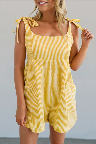 model wearing sleeveless romper in monochromatic yellow vertical pinstripe style pattern with square neckline, tie style wide straps, and relaxed fit high waisted shorts with patch pockets. Shown from the front