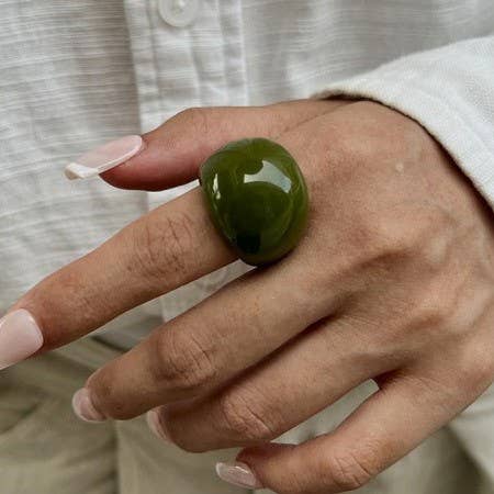 Hand wearing a wide rounded medium green ring made of shiny acrylic resin