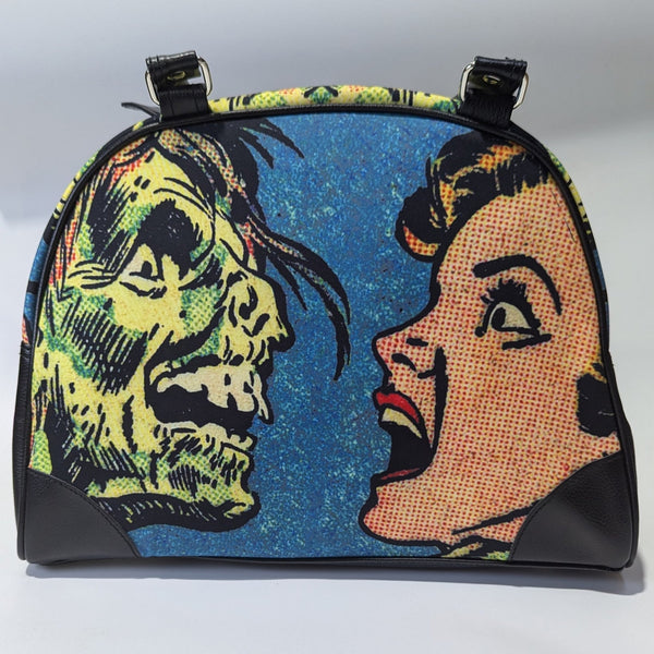 A bowler style purse with a satin body and printed image of comic book Ben Day style  art of a zombie face to face with a screaming woman. The purse has black faux leather handles, protective corners, sides, and bottom. Shown from front with handle lifted to display image