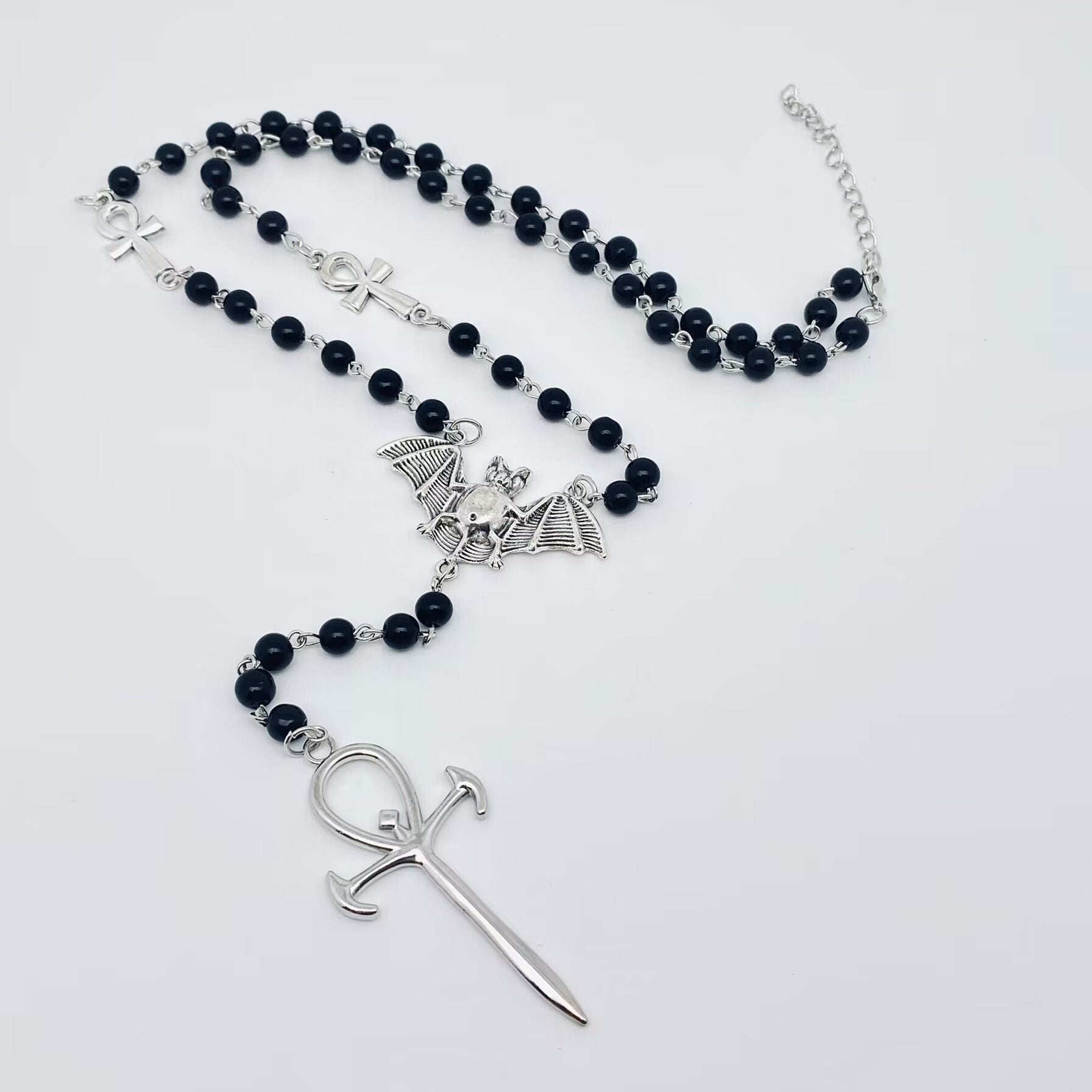 24" black bead rosary-style necklace adorned with shiny silver metal ankh and vampire bat charms, and a 5.5" long center drop finished with a large 2.25" long stylized dagger-like silver metal ankh pendant